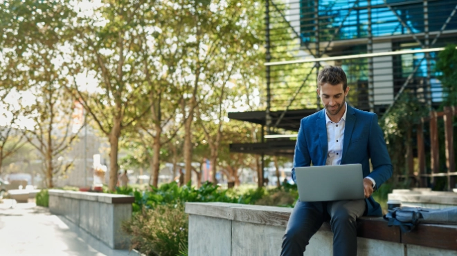 young businessman working online with laptop sitting outside
