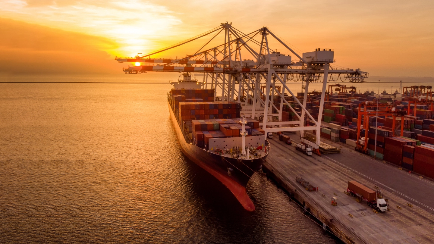 Crane loading container onto container ship at sunset